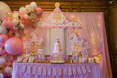 a pink and white carousel themed birthday party with balloons on the ceiling, cake table