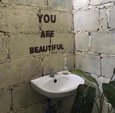 a white sink sitting next to a wall with graffiti on it's side and the words you are beautiful above it