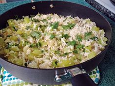 a pan filled with rice and vegetables sitting on top of a blue table cloth next to a knife