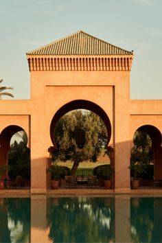 an outdoor swimming pool surrounded by palm trees and stone arches with arched doorways on either side