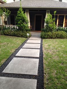 a walkway leading to a house with grass and bushes in the front yard on either side