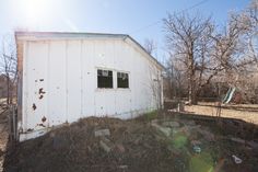 an old white shed sitting in the middle of a field with rocks and grass around it