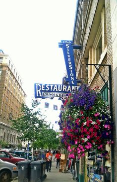 a restaurant sign hanging from the side of a building with flowers in front of it