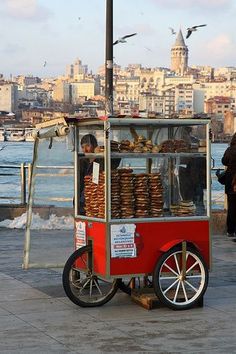 a red cart with donuts on it near the water and buildings in the background