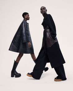 two men walking down the runway in black coats