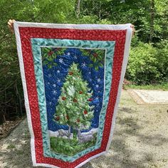 a quilted christmas tree hanging on the side of a road with trees in the background