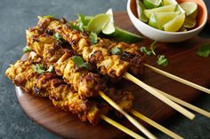 several skewers of food sitting on a wooden plate next to a bowl of lime wedges