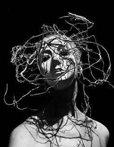 black and white photograph of a woman with branches on her head in front of dark background