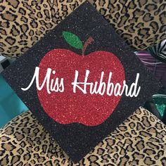 a black and red graduation cap with an apple on it that says miss hubbard