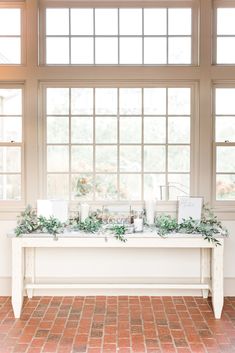 a long table with candles and greenery on it in front of large windows at the reception