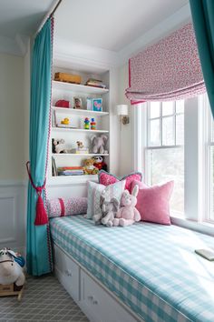 a child's bedroom with blue curtains and pink pillows on the window sill