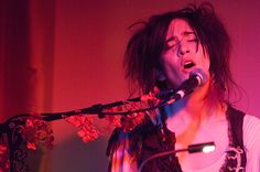 a woman singing into a microphone in front of a microphone stand with flowers on it