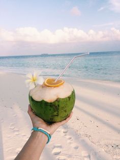 a person holding up a coconut drink on the beach