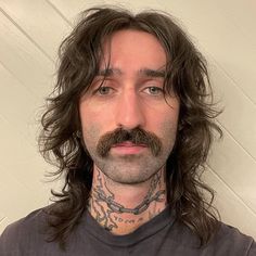 a man with long hair and tattoos on his face is looking at the camera while wearing a t - shirt