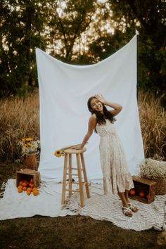 a woman standing next to a wooden stool in front of a white backdrop with sunflowers