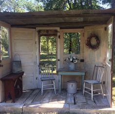 a small shed with chairs and a table in the front yard, next to an open door