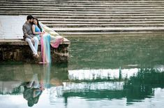 a man and woman sitting on the edge of a body of water next to some steps