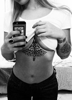 a woman with tattoos on her stomach holding a cell phone in front of her chest