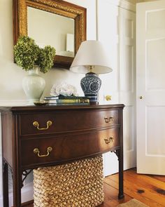 a wooden dresser with a lamp on top of it next to a mirror and vase