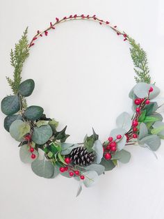 a christmas wreath with red berries, greenery and pine cones