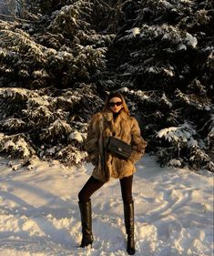 a woman standing in the snow wearing boots and a fur coat with her hands on her hips