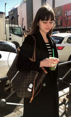 a woman in black holding a brown purse and a drink with her hand on her hip