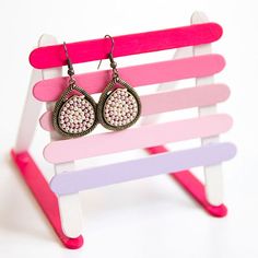 a pair of pink and purple earrings sitting on top of a wooden stand