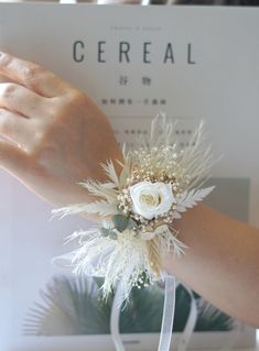 a woman's hand holding a white flower and feather corsage on her wrist