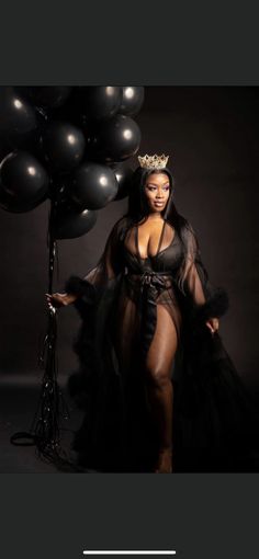 a woman in a black dress and crown standing next to balloons with her hands on her hips