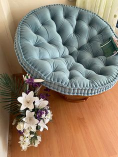 a blue round couch sitting on top of a wooden floor next to a vase with flowers