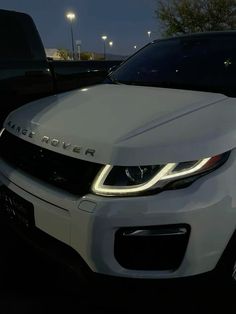 the front end of a white range rover parked in a parking lot at night with its lights on