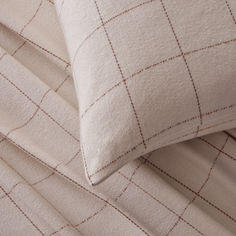 two pillows sitting on top of each other with white and brown checkered sheets in the background