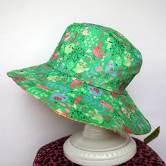 This green & orange reversible sun hat is handmade (by me) using high quality 100% cotton fabric. One side is mint green with a retro bird print and the other side is orange with a matching bird print.  It has a wide 8cm brim. This is available in girls and ladies sizes and is completely machine washable. The brim is fairly stiff so it doesn't flop in your face, but it will soften slightly with use.   These are the sizes I have available. Please click on the options above to see what I have left Playful Green Sun Hat For Spring, Playful Green Brimmed Sun Hat, Fun Green Sun Hat For Summer, Whimsical Green Summer Hats, Playful Adjustable Reversible Sun Hat, Playful Green Hat For Summer, Playful Green Brimmed Bucket Hat, Green Reversible Cotton Bucket Hat, Playful Green Wide Brim Hat