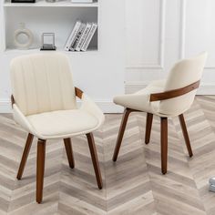 two white chairs sitting next to each other on top of a hard wood floor in front of a book shelf