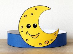 a yellow crescent with black eyes and a smile on it's face is sitting on a blue ribbon