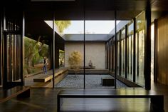 the inside of a house with glass walls and wood flooring, as well as a woman standing in the doorway