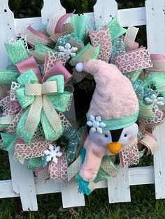 a pink and green christmas wreath with a snowman on the front, attached to a white picket fence