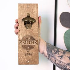 a man holding up a bottle opener with the smiths logo on it, in front of a white wall