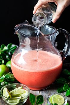 someone pouring water into a pitcher filled with fruit