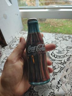 a person holding up a coca - cola bottle in front of a window