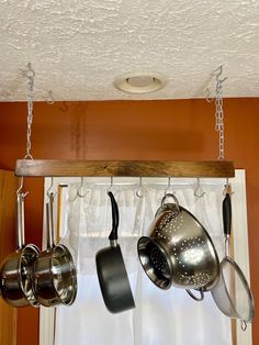 pots and pans hanging from hooks on a window sill in front of curtains