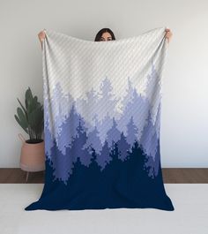 a woman is holding up a blue and white blanket in front of a potted plant