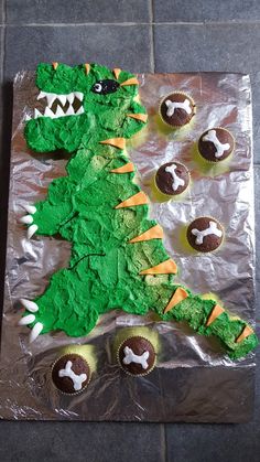 a cake shaped like a dinosaur with cupcakes on it