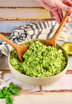 a bowl full of guacamole with a wooden spoon in it and someone's hand on the side