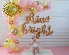 a baby is sitting in front of some balloons with the words shine bright on it