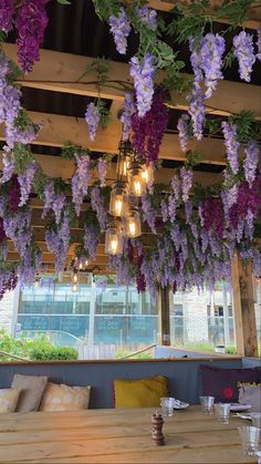 purple flowers are hanging from the ceiling above a wooden dining table in a restaurant with large windows