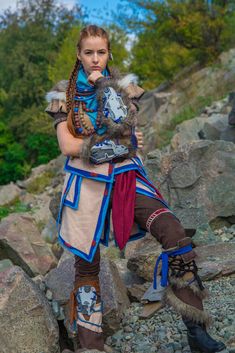 a woman dressed in costume standing on rocks with her arms around her neck and looking at the camera