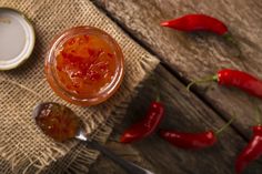 a glass jar filled with jam sitting on top of a wooden table next to two spoons