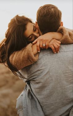 a man and woman embracing each other in the middle of an open field with brown grass