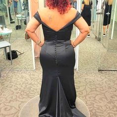 a woman standing in front of a mirror wearing a black dress with an open back